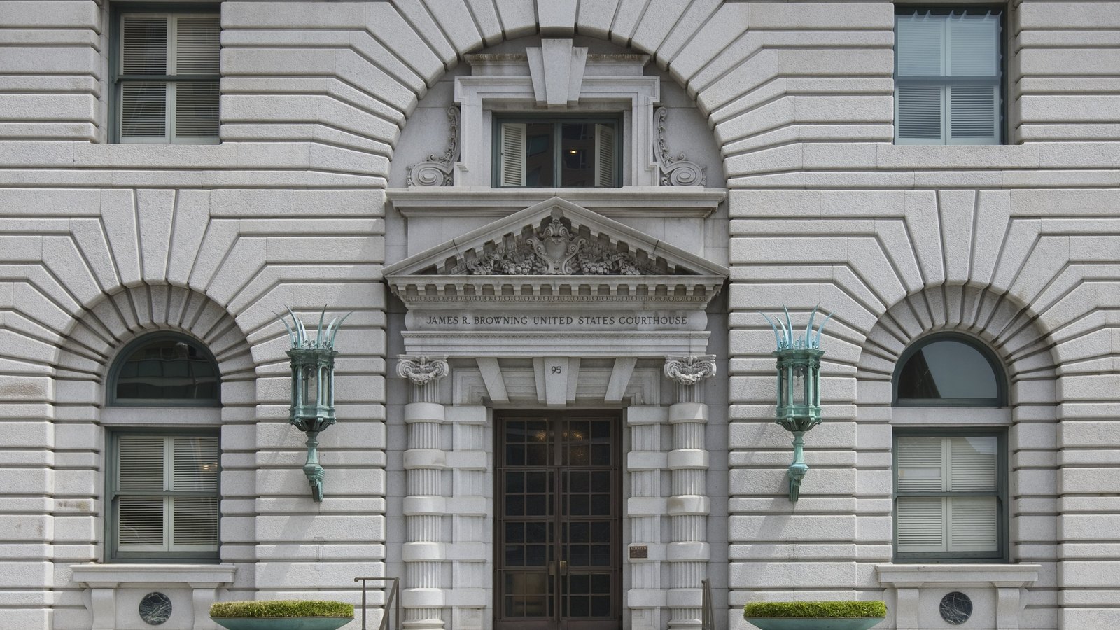 Façade en pierre claire du James R. Browning U.S. Courthouse à San Francisco, avec une porte sous un fronton sculpté, deux lanternes vertes et des fenêtres en arc