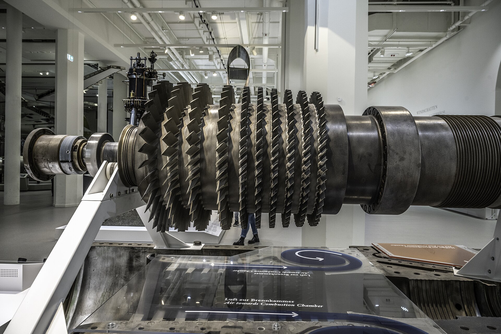 Grand rotor de compresseur de turbine à gaz exposé sur un support dans un hall de musée, avec ses rangées d'aubes métalliques