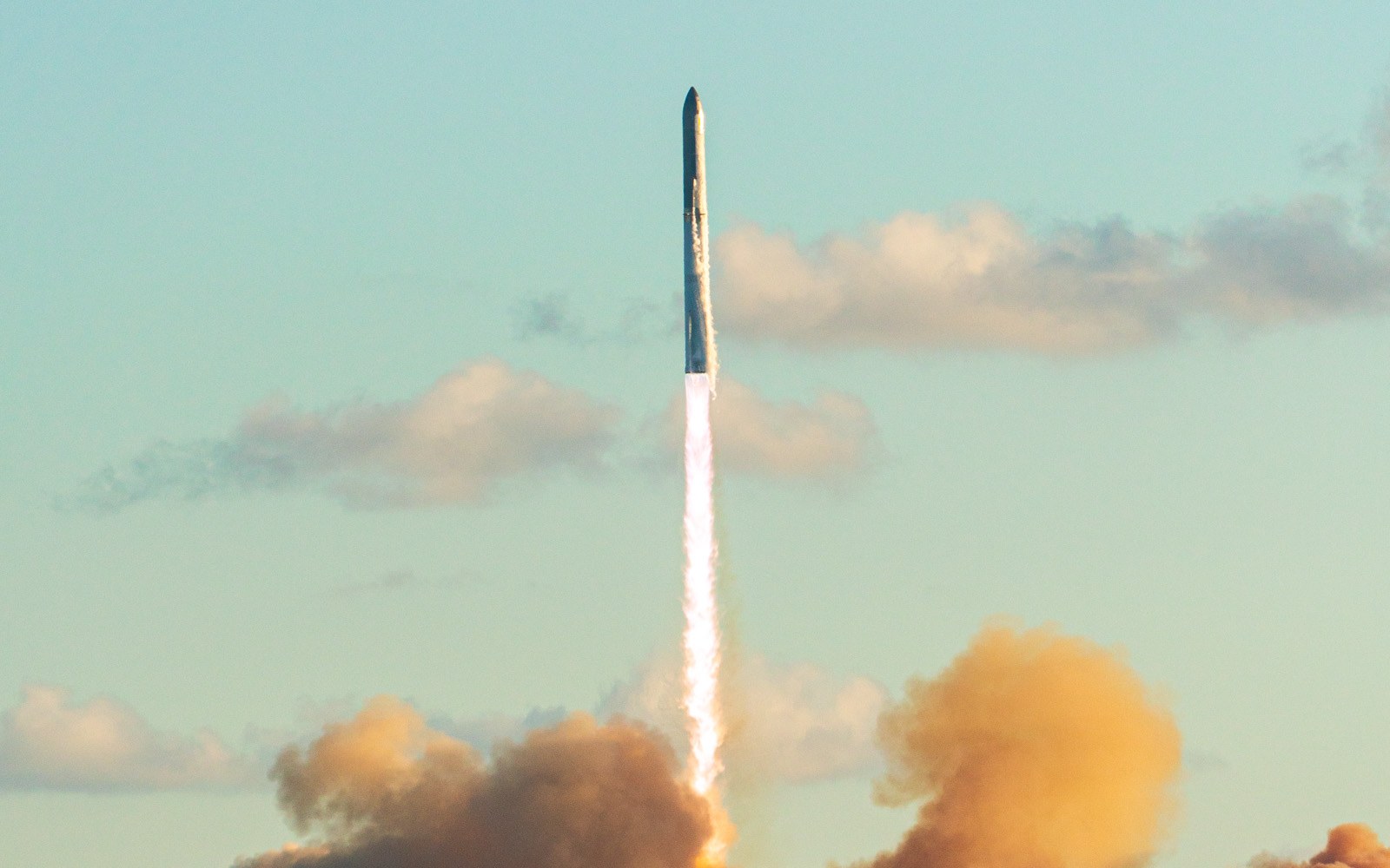 La fusée Starship de SpaceX s'élève au-dessus d'un épais nuage de fumée orangée à Starbase, au Texas, dans un ciel bleu