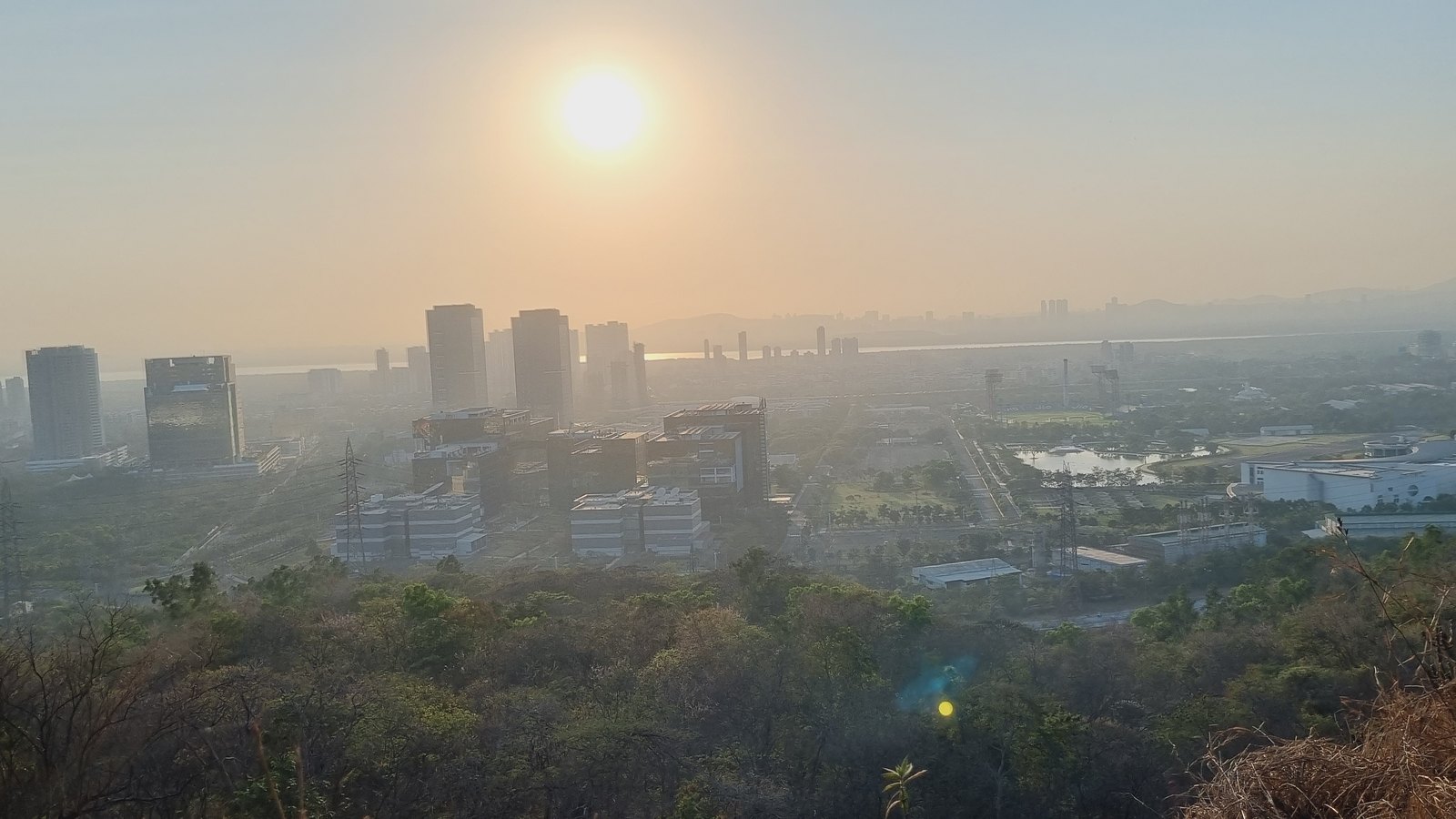 Vue en hauteur sur des tours de bureaux et des bâtiments du site de Reliance Jio à Navi Mumbai, au coucher du soleil, avec une colline boisée au premier plan