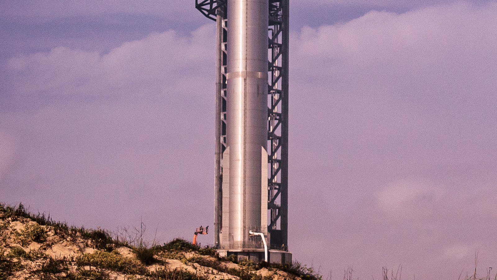 Le premier étage Super Heavy de Starship, cylindre en acier, dressé sur le pas de tir orbital contre la tour de lancement de Starbase au Texas