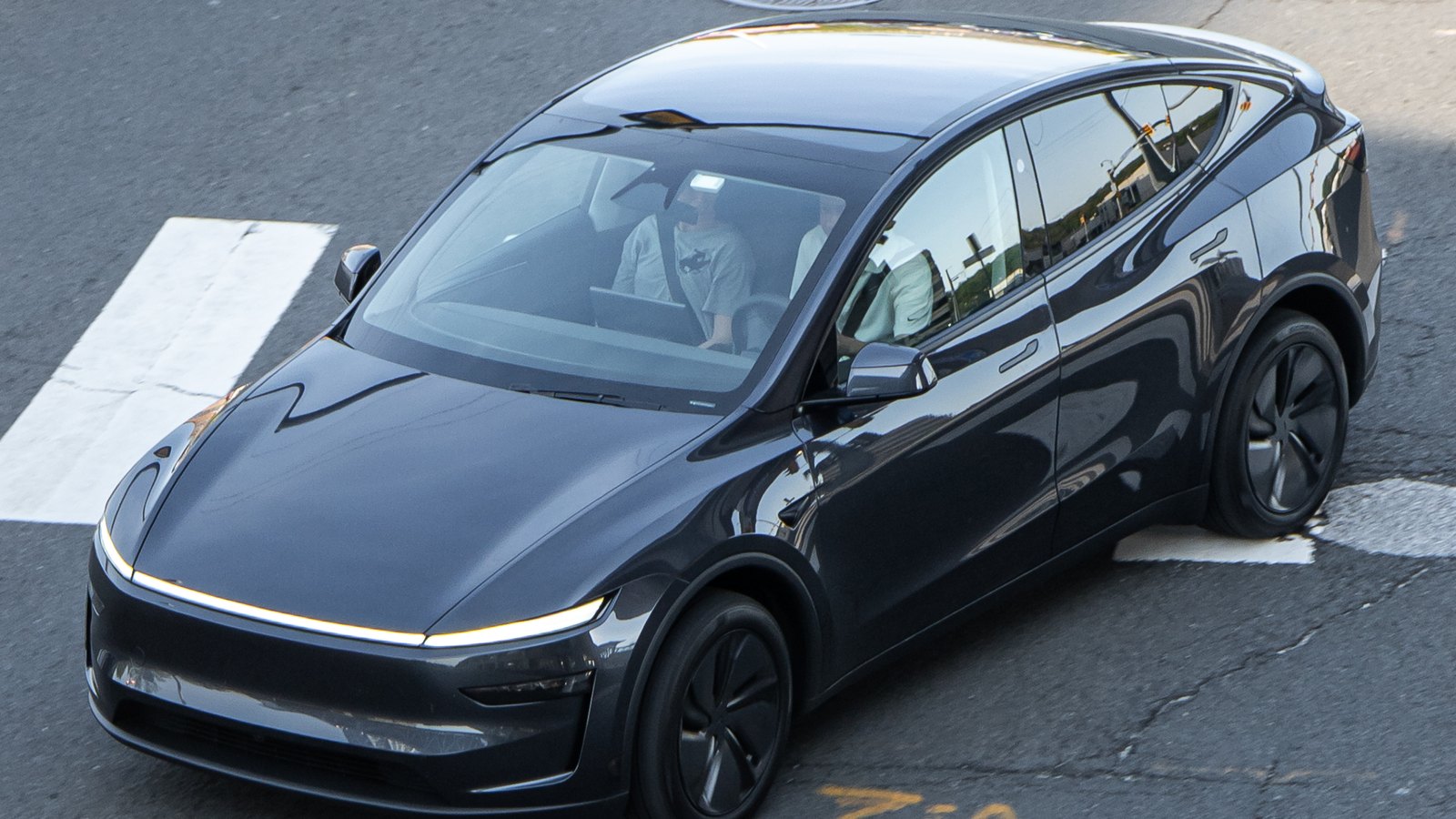 Un Tesla Model Y restylé de couleur gris foncé vu de haut, traversant un carrefour près de Washington