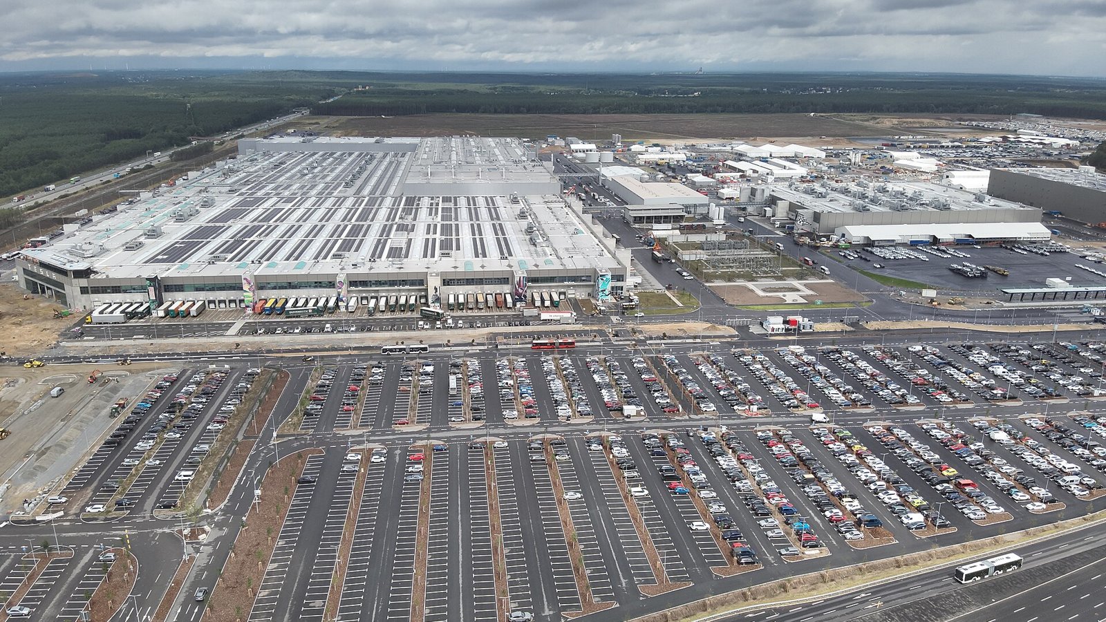 Vue aérienne de l'usine Tesla de Grünheide près de Berlin, avec ses grands bâtiments blancs et des parkings remplis de voitures