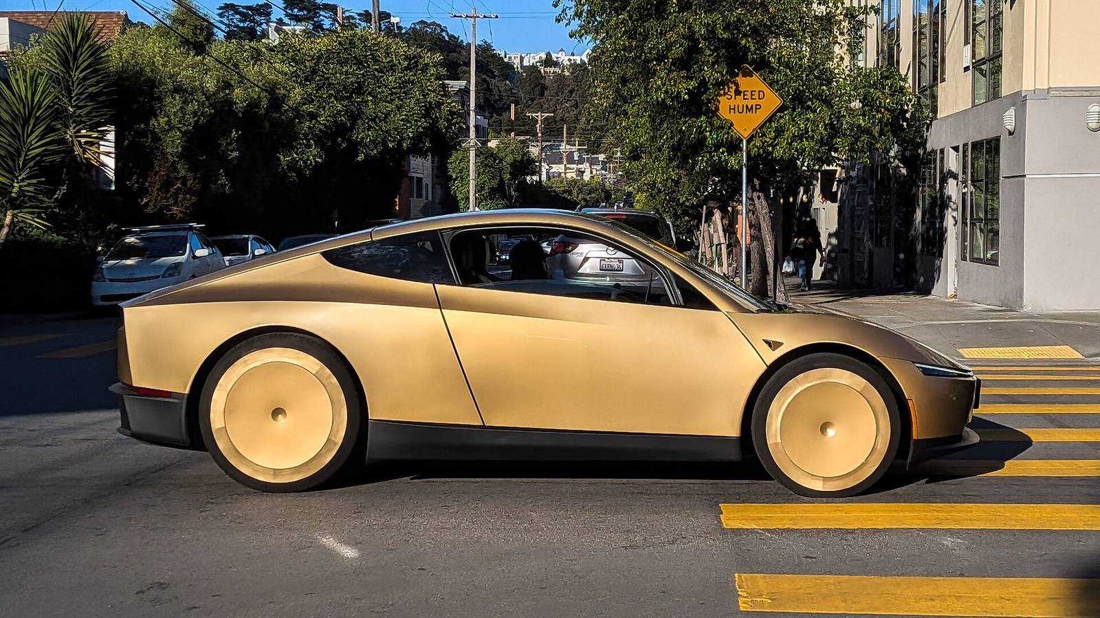 Un Cybercab Tesla doré à deux places roule dans une rue ensoleillée de San Francisco près d'un panneau jaune Speed Hump